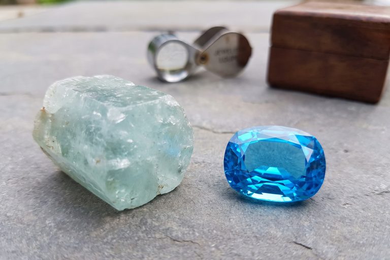 a soft sea-green aquamarine with a faint internal veil, and beside it a vivid electric-blue topaz with sharper saturation