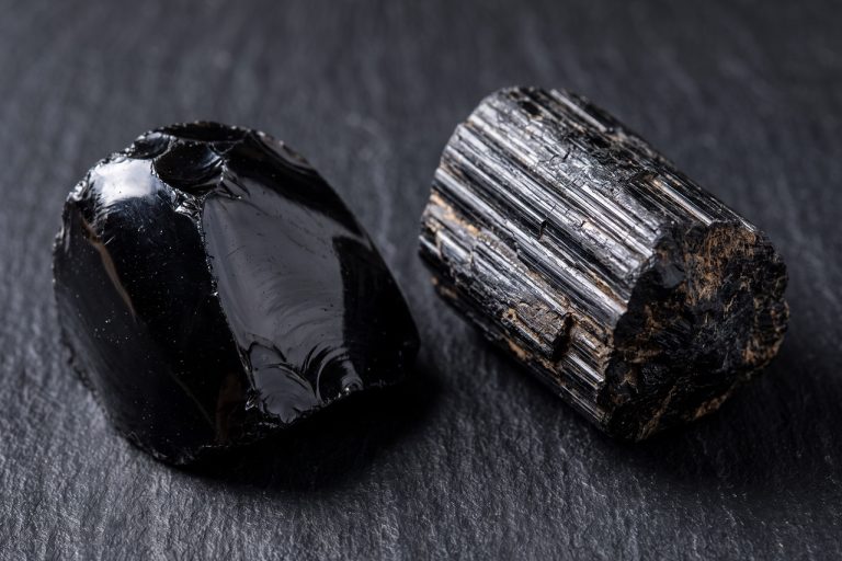 A glossy black obsidian mass with a smooth conchoidal fracture surface sits beside a stubby black tourmaline prism