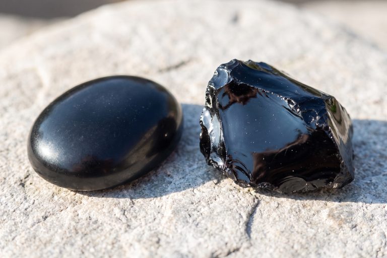 A polished solid-black onyx cabochon sits beside a glossy black obsidian