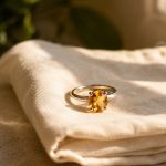 Citrine ring with silver band on folded linen beside glass of water in warm morning light