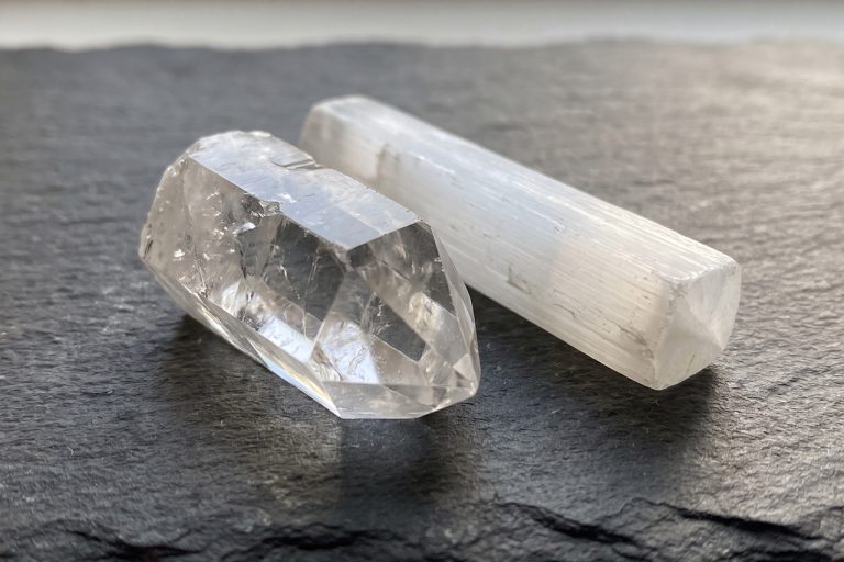 A clear six-sided quartz point with internal veils sits beside a pearly white selenite