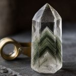 Transparent quartz crystal with green chlorite phantom on slate beside a brass loupe.