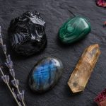 A raw black obsidian piece, a tumbled malachite, a polished labradorite cabochon showing blue flash, and a citrine point