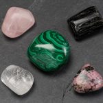 A tumbled malachite at center surrounded by companion stones — rose quartz, black tourmaline, clear quartz, rhodonite