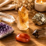 A citrine point at center surrounded by companion stones — clear quartz, pyrite, amethyst, carnelian, smoky quartz — on a warm golden-toned wooden surface