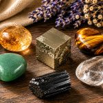 A pyrite cube at center surrounded by companion stones — citrine, tiger's eye, green aventurine, clear quartz, black tourmaline — on a dark wooden surface