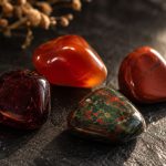 Polished garnet, carnelian, red jasper, and bloodstone on a black slate surface in warm window light