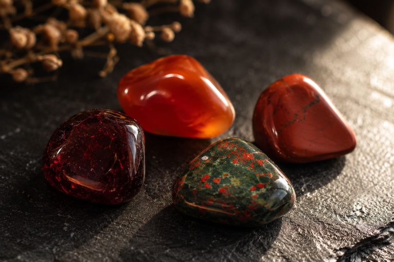 Polished garnet, carnelian, red jasper, and bloodstone on a black slate surface in warm window light