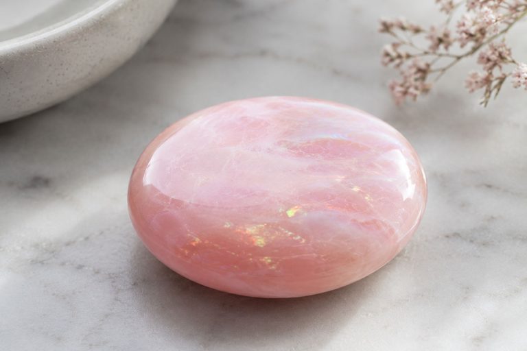 Polished pink rose quartz crystal on marble surface for healing and meditation.