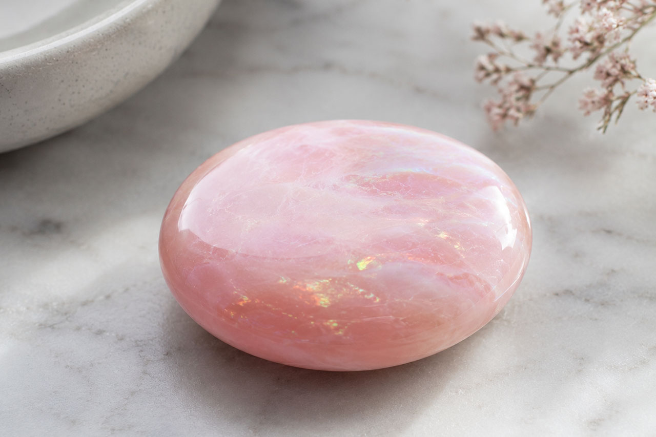 Polished pink rose quartz crystal on marble surface for healing and meditation.