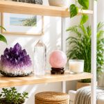 Bright living room shelf with an amethyst cluster, clear quartz point, rose quartz sphere, plants, and an unlit candle in warm afternoon sunlight